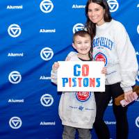 Young boy holding a "Go Pistons" sign posting for photo with young woman